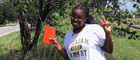 Blogger Nailah Johnson '24 posing with an orange research notebook in a rural area