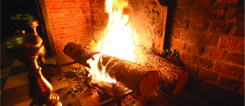 Yule logs burning in a large brick fireplace with sprigs of holly tossed around the logs
