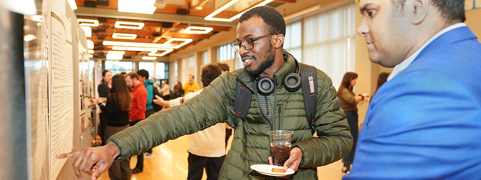 A poster presenter talks to a person who is pointing and looking at their research poster.