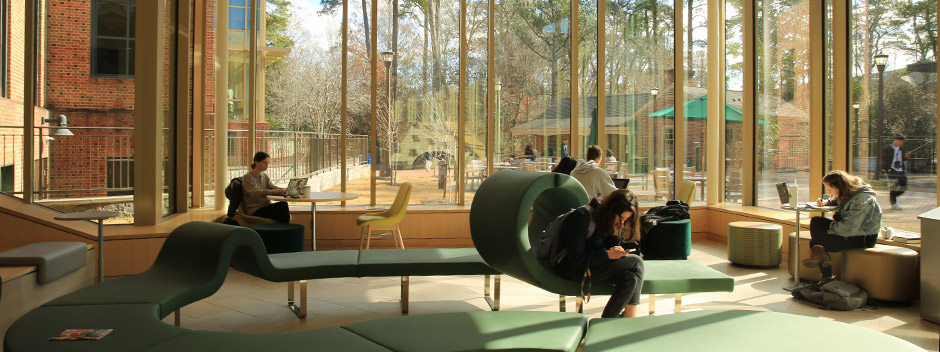 Students studying in front of a two-story window with campus beyond