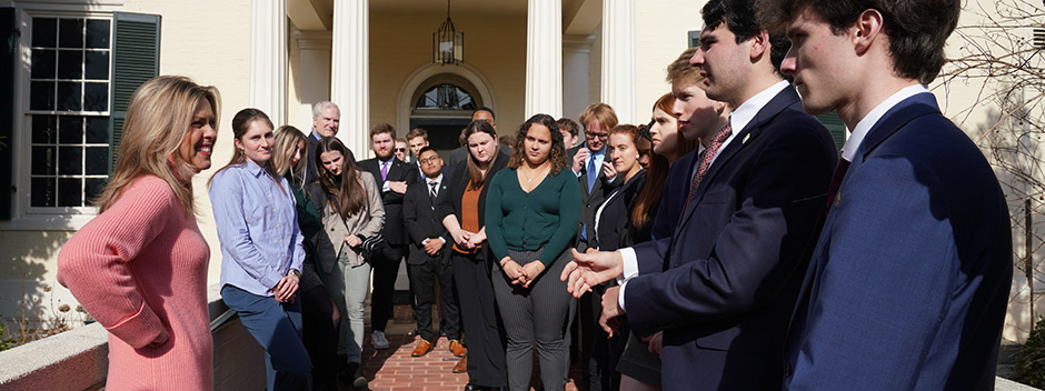 A group of students in professional attire stand outside of the Executive Mansion talking with First Lady of Virginia Suzanne S. Youngkin