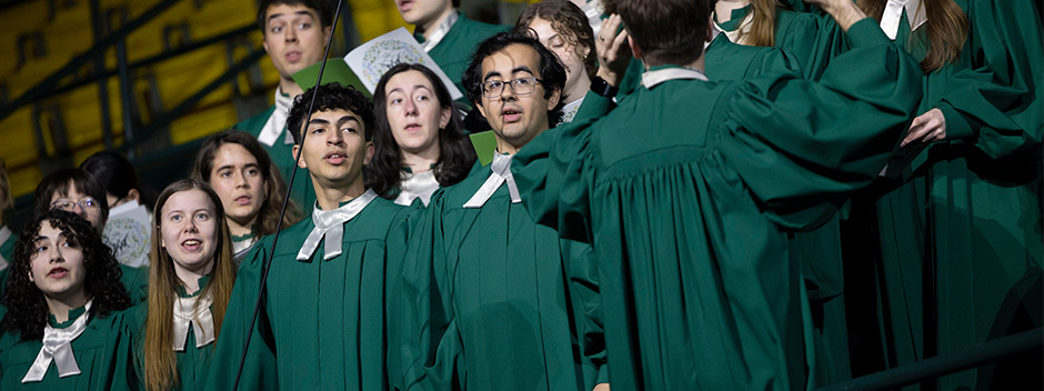 Members of the W&amp;M Choir sing in green robes and white collars in Kaplan Arena