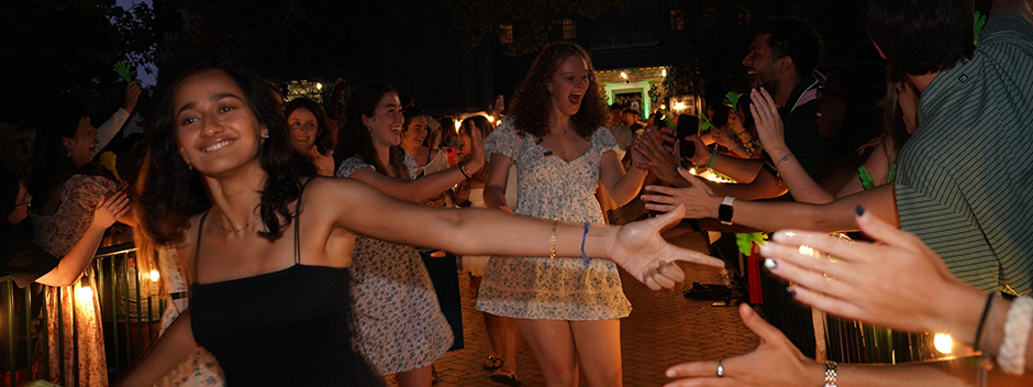 New students are high-fiving and waving to the crowd as they walk through the Wren Courtyard and the cheering W&amp;M community at night.