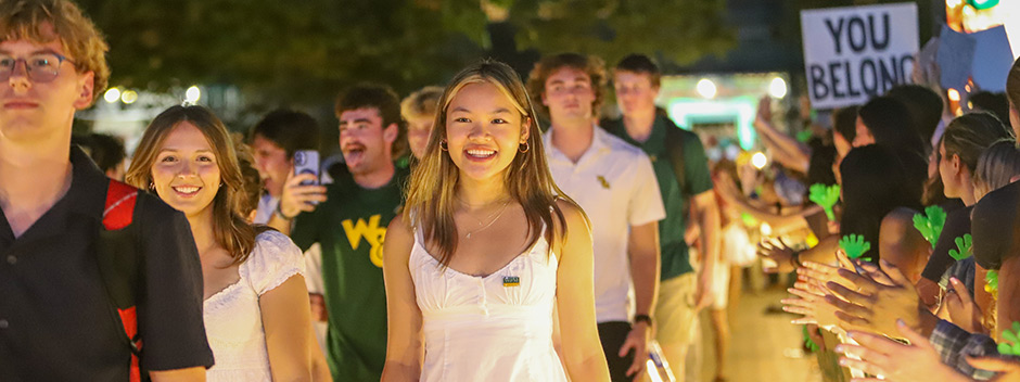 Smiling students walk through the Wren Courtyard and the cheering W&amp;M community at night. 
