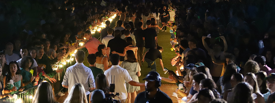 A view at night from behind and above as new students walk down the brick walkway of the Wren Courtyard through cheering members of the W&amp;M community on either side.