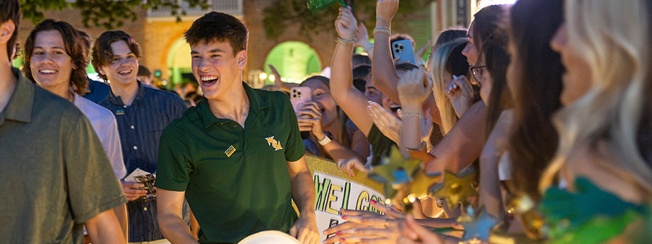 Smiling students walk through the Wren Courtyard and the cheering W&amp;M community at night. 