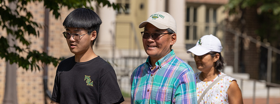 A family smiles and walks across campus with brick buildings in the background