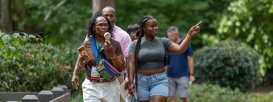 A smiling student points as they walk with their family across old campus