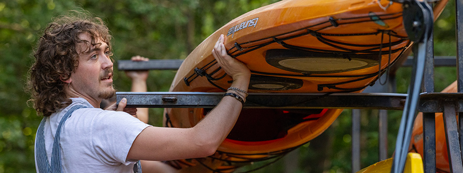 A person in overalls hoists a kayak on a rack