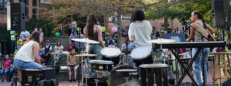 Students perform on an outdoor stage with families and students watching on the Sadler Terrace