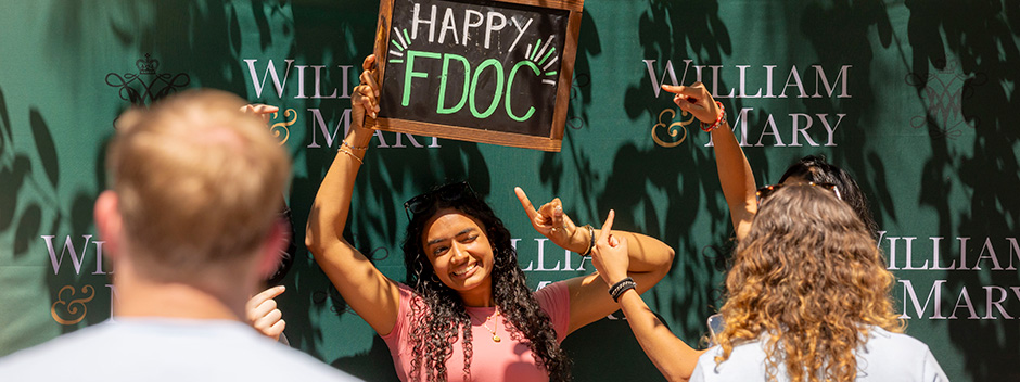 A smiling student holding a chalkboard sign with the lettering Happy FDOC as onlookers take pictures and point