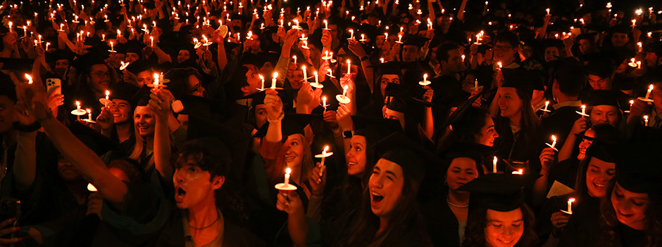 Crowd of graduates at night holding candles and singing
