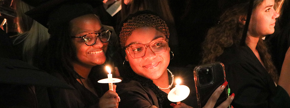 Crowd of graduates at night holding candles and singing
