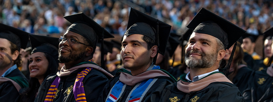 Graduates in commencement attire listening and smiling