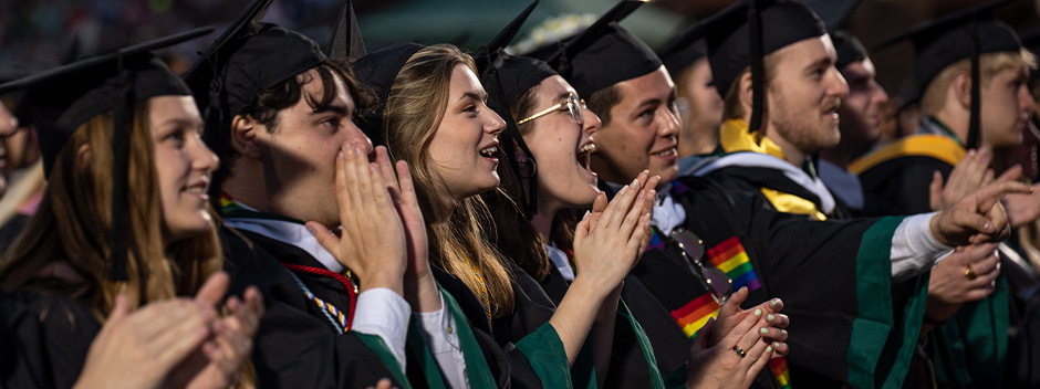 Graduates in commencement attire smiling and cheering