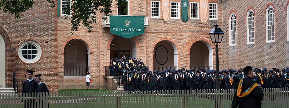 Graduates in commencement attire walking through the historic Wren Building