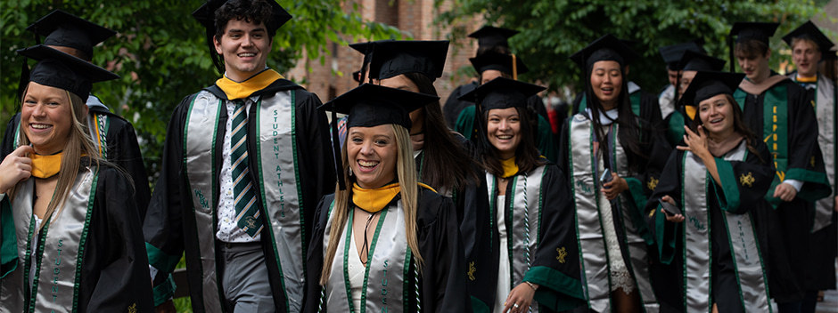 Graduates in commencement attire walking across campus