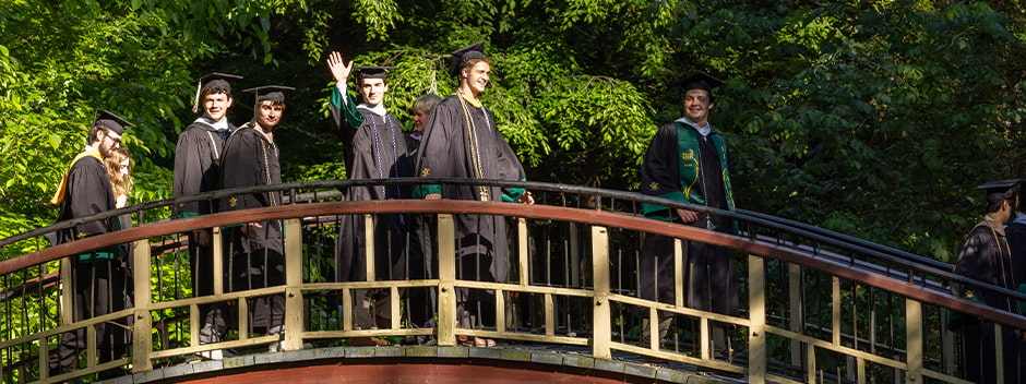 Graduates in full regalia walk across the Crim Dell bridge