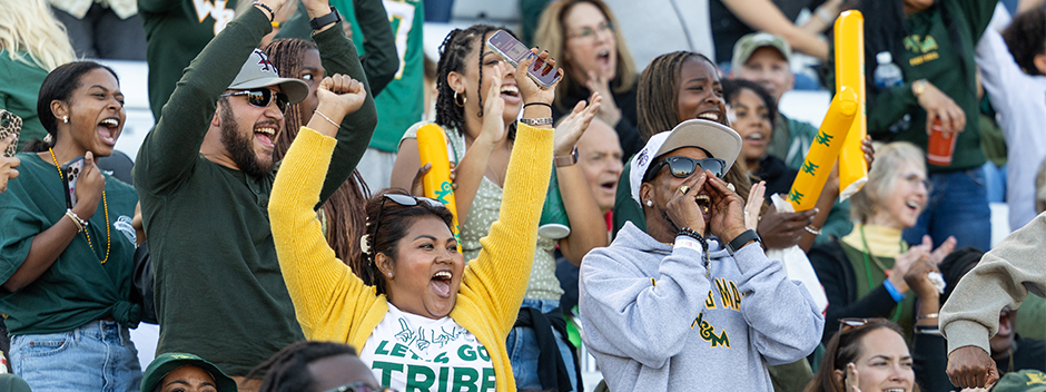 Smiling students cheering on the Tribe and waving boom sticks at the homecoming football game in Zable Stadium on a sunny day
