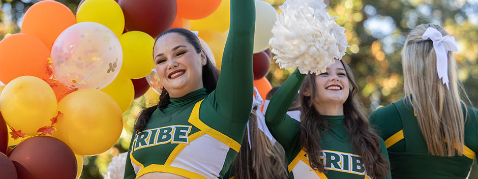 Tribe cheerleaders wave pompoms as they process in the parade surrounded by colorful balloons