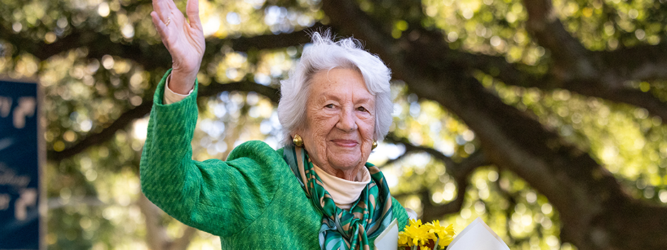 Grand Marshal Jane Batten waving with trees in the background on a sunny day