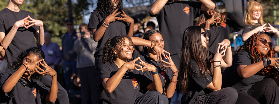 Smiling members of the Syndicate Hip Hop dance group pose with matching William & Mary hand gestures during their performance at the parade