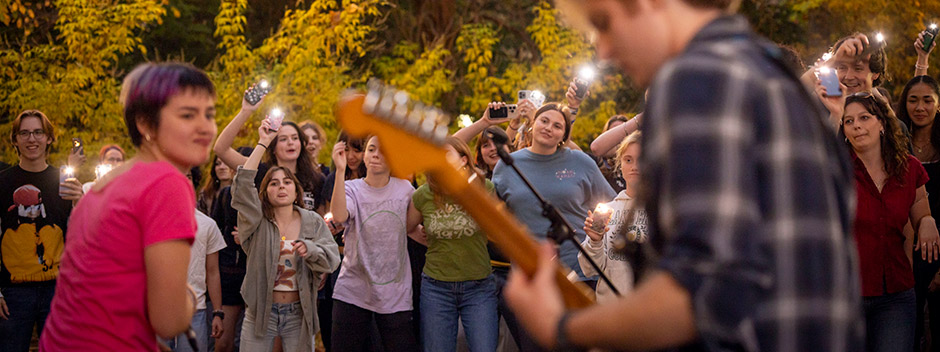 Students cheer on with lit cell phones as they watch a band performing in the foreground
