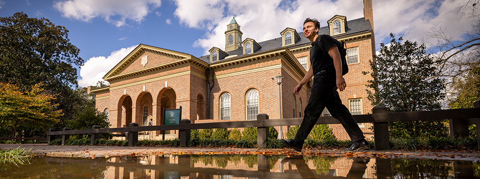On a sunny fall da student walks near a puddle reflecting a view of Tucker Hall in the background