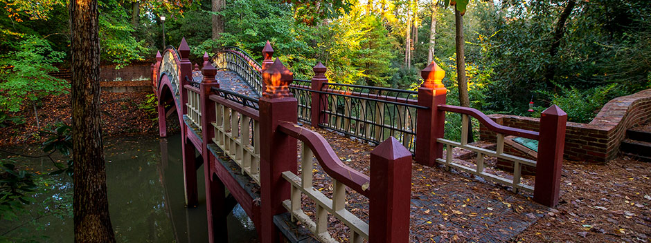 Red, white and black painted foot bridge over the small Crim Dell with fall foliage dropping from the surrounding trees