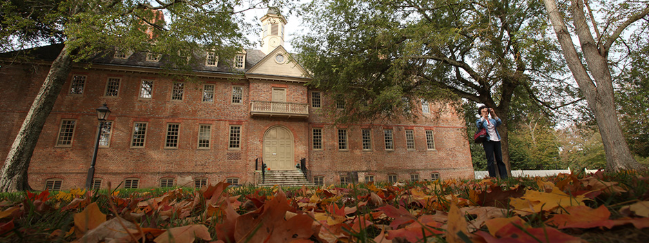 Historic brick Wren Building with brown leaves of fall covering the grassy lawn in the foreground