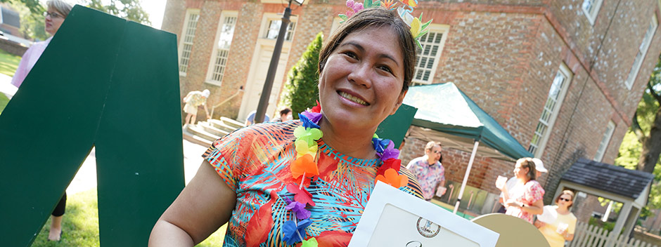 An employee poses near the Wren Building with a large W&amp;M sign