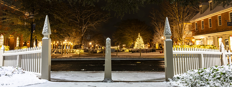 An inch of snow covers the streets and brick shops in a view through white gate posts and down Duke of Gloucester Street still lit for the holidays