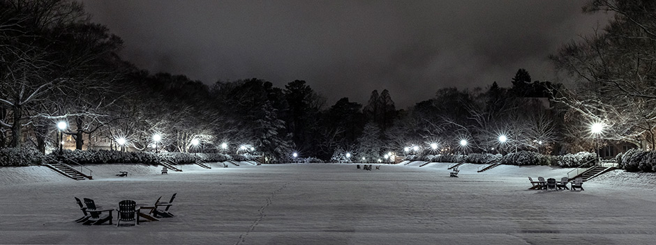 A few inches of snow covering the Sunken Garden at night with Adirondack chairs still grouped together throughout the scene