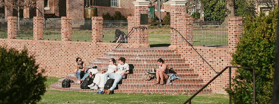 A group of four students relax between classes on the semi-circle of brick steps that lead out of the Sunken Garden