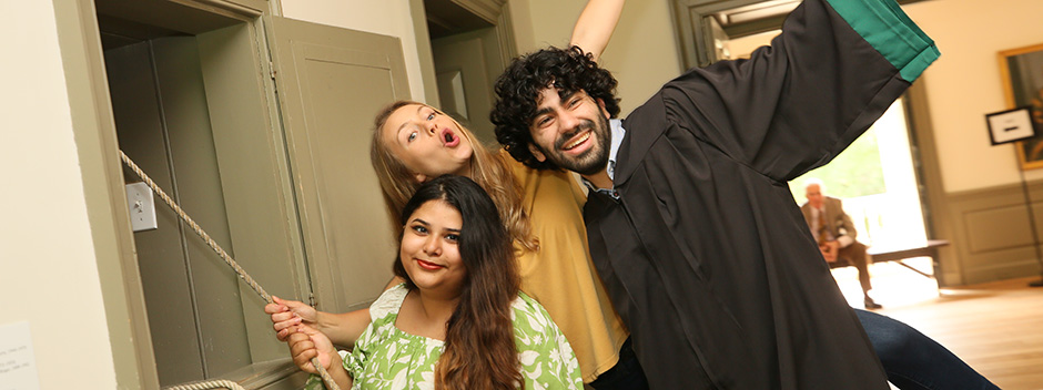 Three graduates pose while ringing the Wren Bell