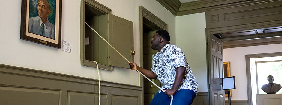 A smiling student pulls a rope in the Wren Building to ring the Wren Bell