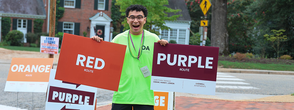 A smiling Orientation Aid holding directional signs for color-coded move-in routes
