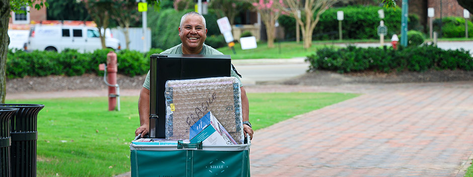 A smiling family member pushes a rolling cart along a brick pathway