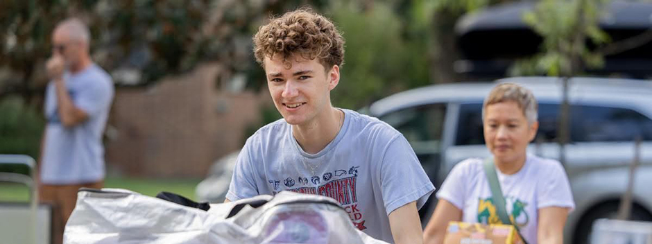 A student pushing a cart of belongings at move-in with family members in the background