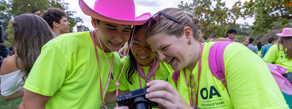 Three orientation aides smiling and looking at photos on a camera in Colonial Williamsburg